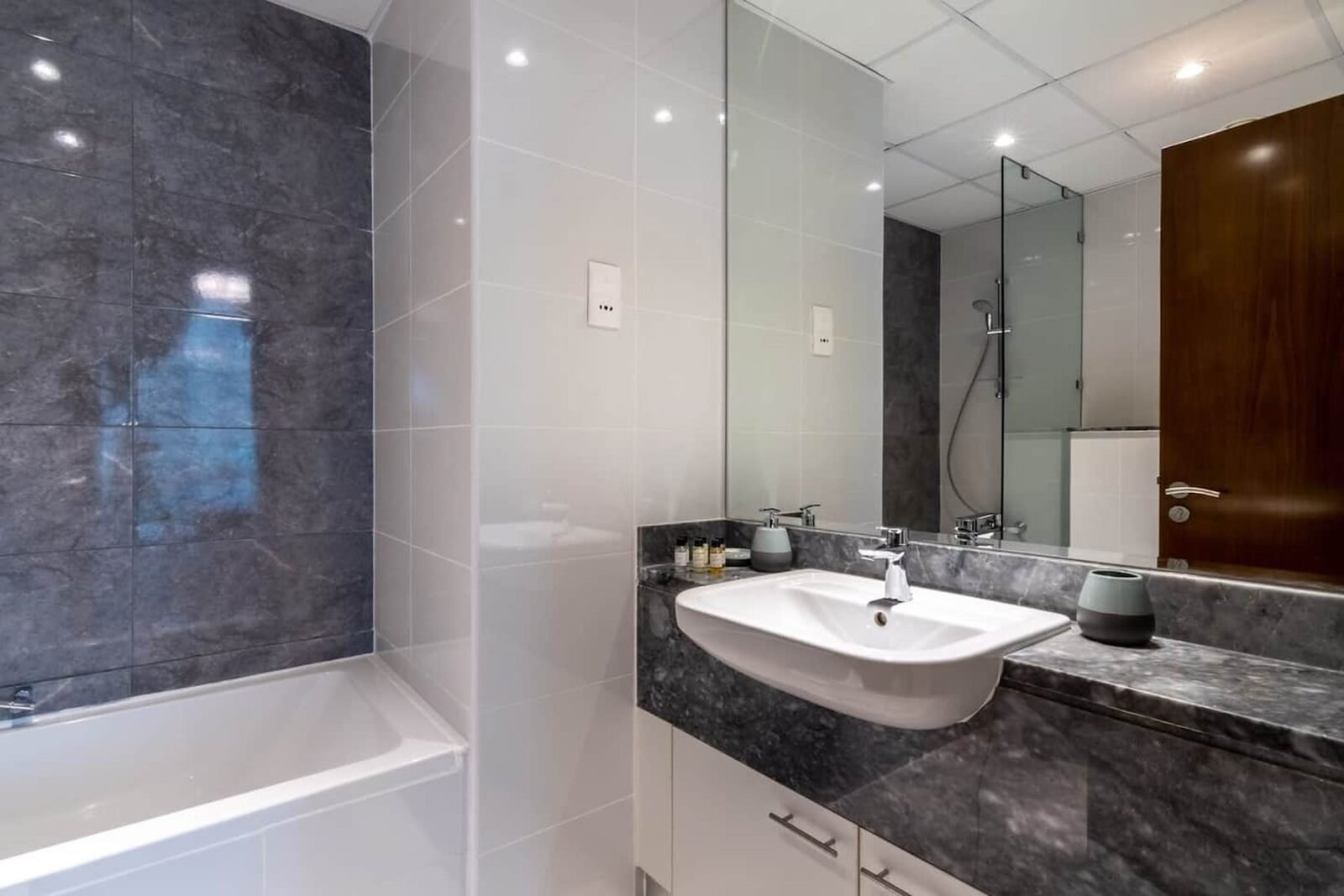 Grey marble bathroom with white gloss vanity, mirrored wall and bath