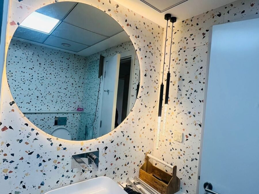Terrazzo guest bathroom with round backlit mirror and navy vanity