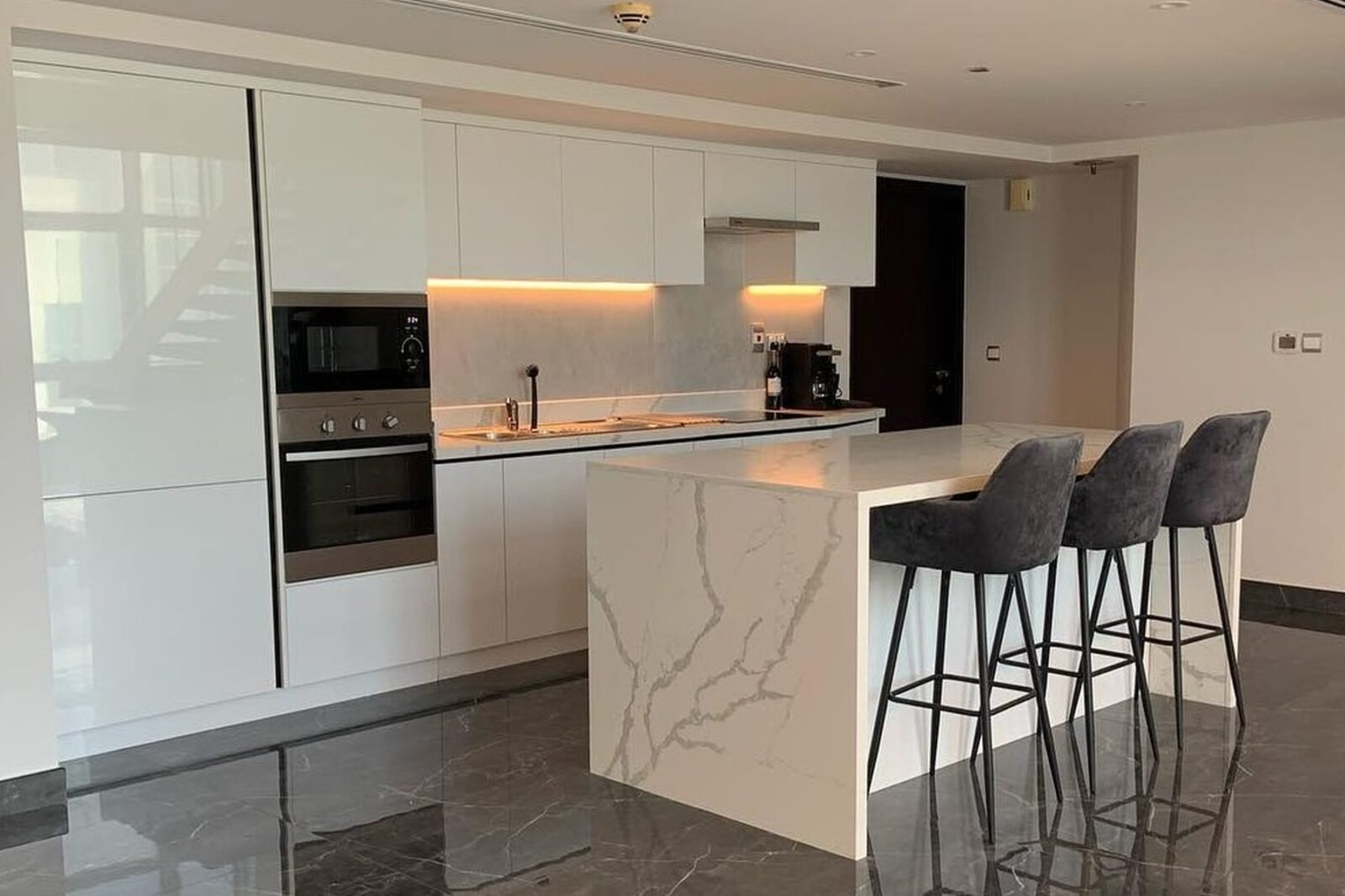 Handleless white kitchen with marble-effect waterfall island and three bar stools