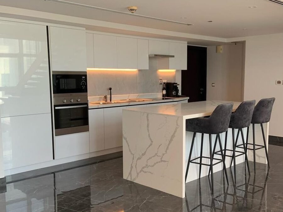 Handleless white kitchen with marble-effect waterfall island and three bar stools
